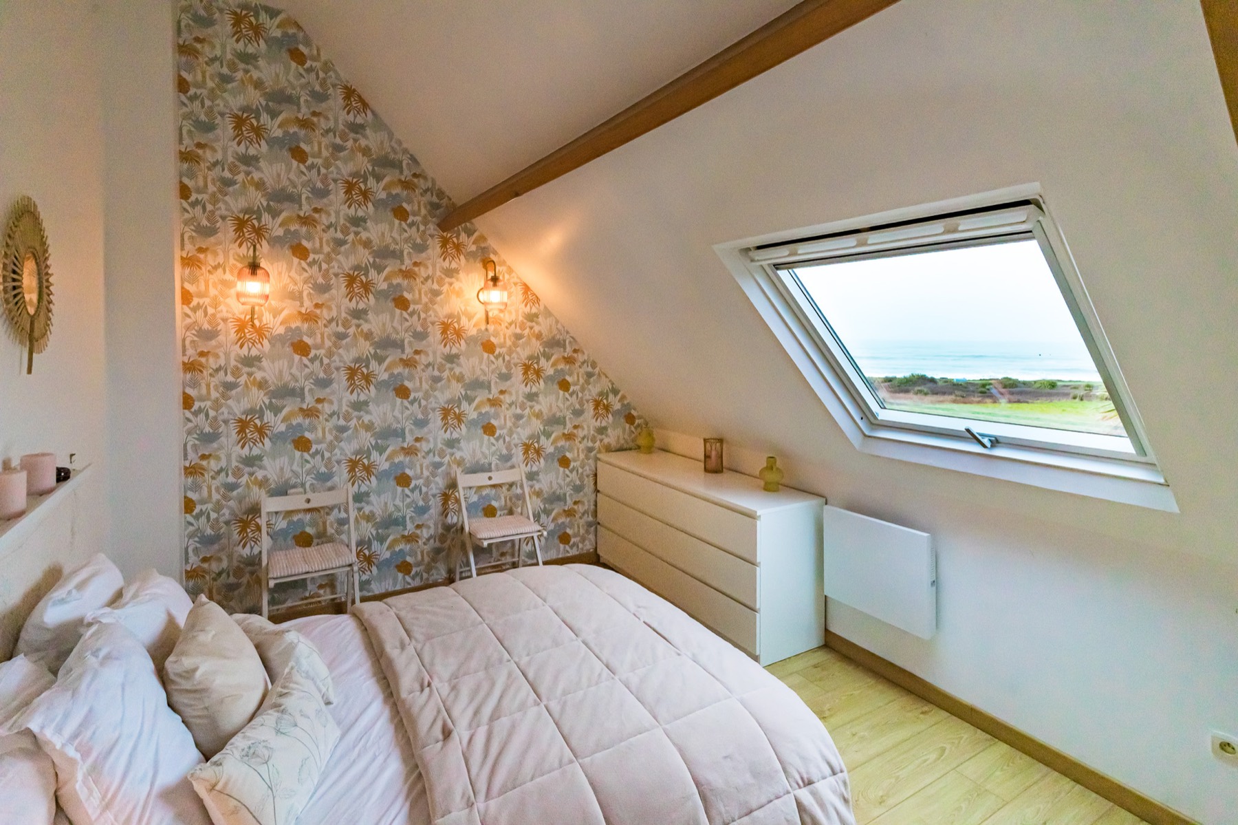 Chambre mansardée avec grande fenêtre ouverte sur la mer